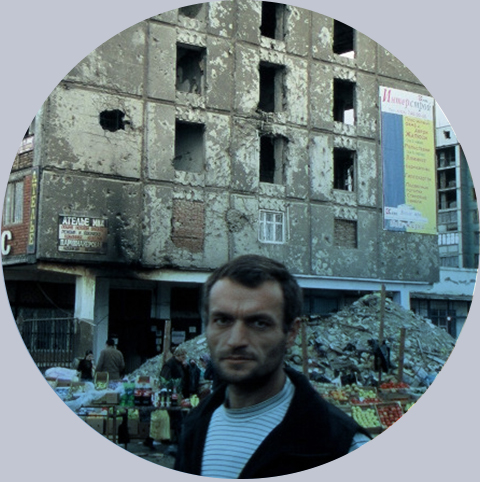 Mężczyzna na tle zrujnowanego wojną bloku w Groznem. Fot.: PAH