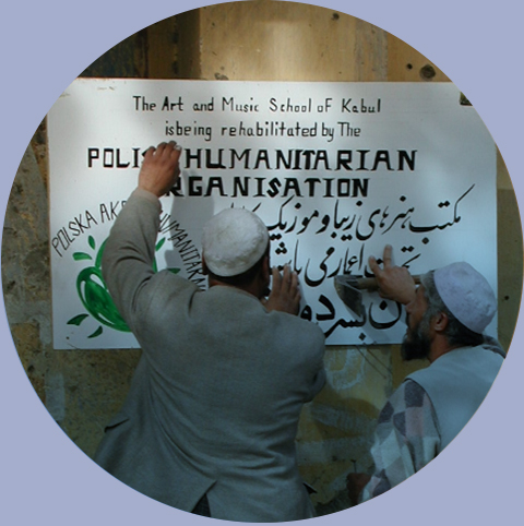 Dwóch Afgańczyków wiesza tablicę z informacją i logiem Polskiej Akcji Humanitarnej na szkole artystyczno-muzycznej, Kabul. Fot.: PAH