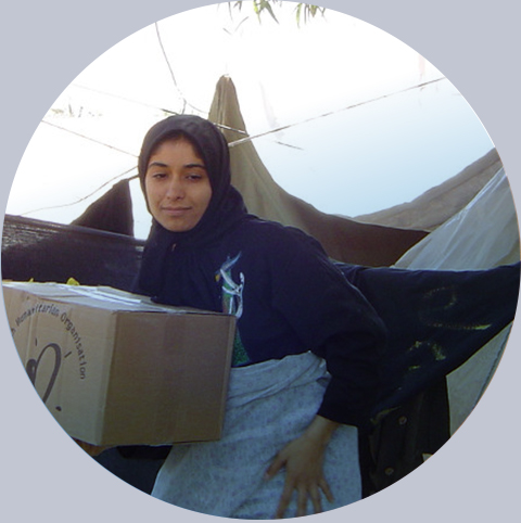 Dziewczynka w chuście przy namiotach trzyma paczkę z logo Polskiej Akcji Humanitarnej, Bam Iran 2004 rok. Fot.: PAH