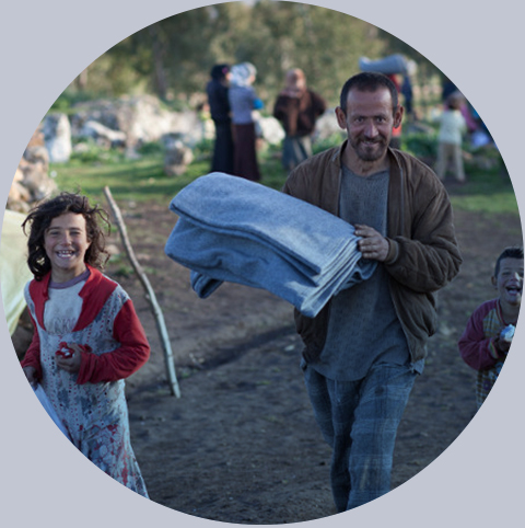 Uśmiechnięty męczyzna z dwójką dzieci ubrancych w wysłużone ubrania niosą koce i detergenty, otrzymana pomoc uchodźcy wewnątrz Syrii, wojna Idlib, 2013. Fot:. Maciej Moskwa
